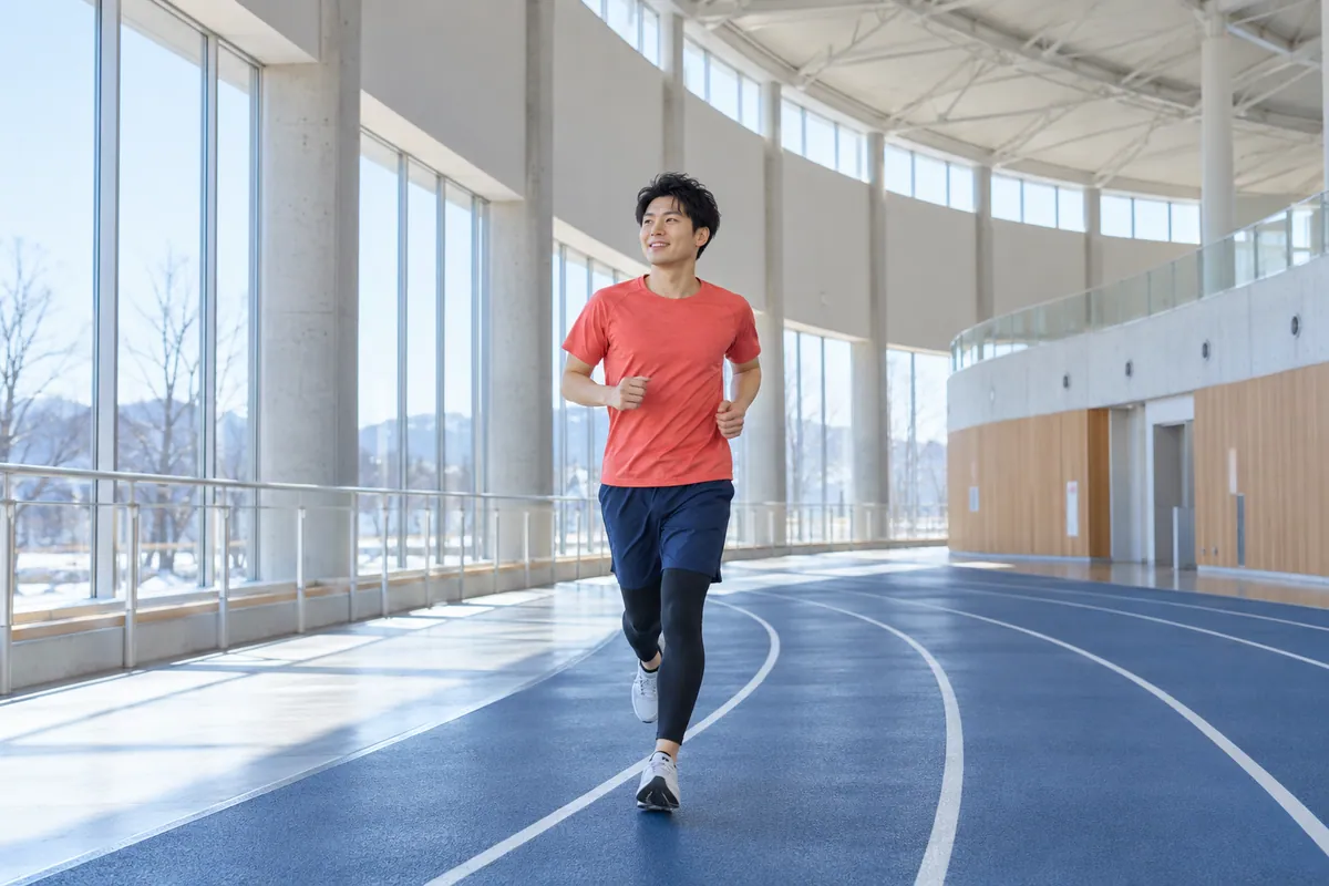 架空の公共スポーツ施設の屋内コースを、若い成人男性が無理のないペースで走るイメージ。